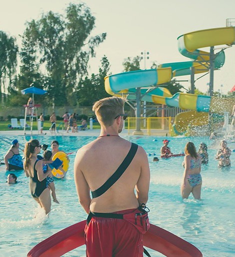 lifeguard standing with his back to the camera looking over a pool full of people
